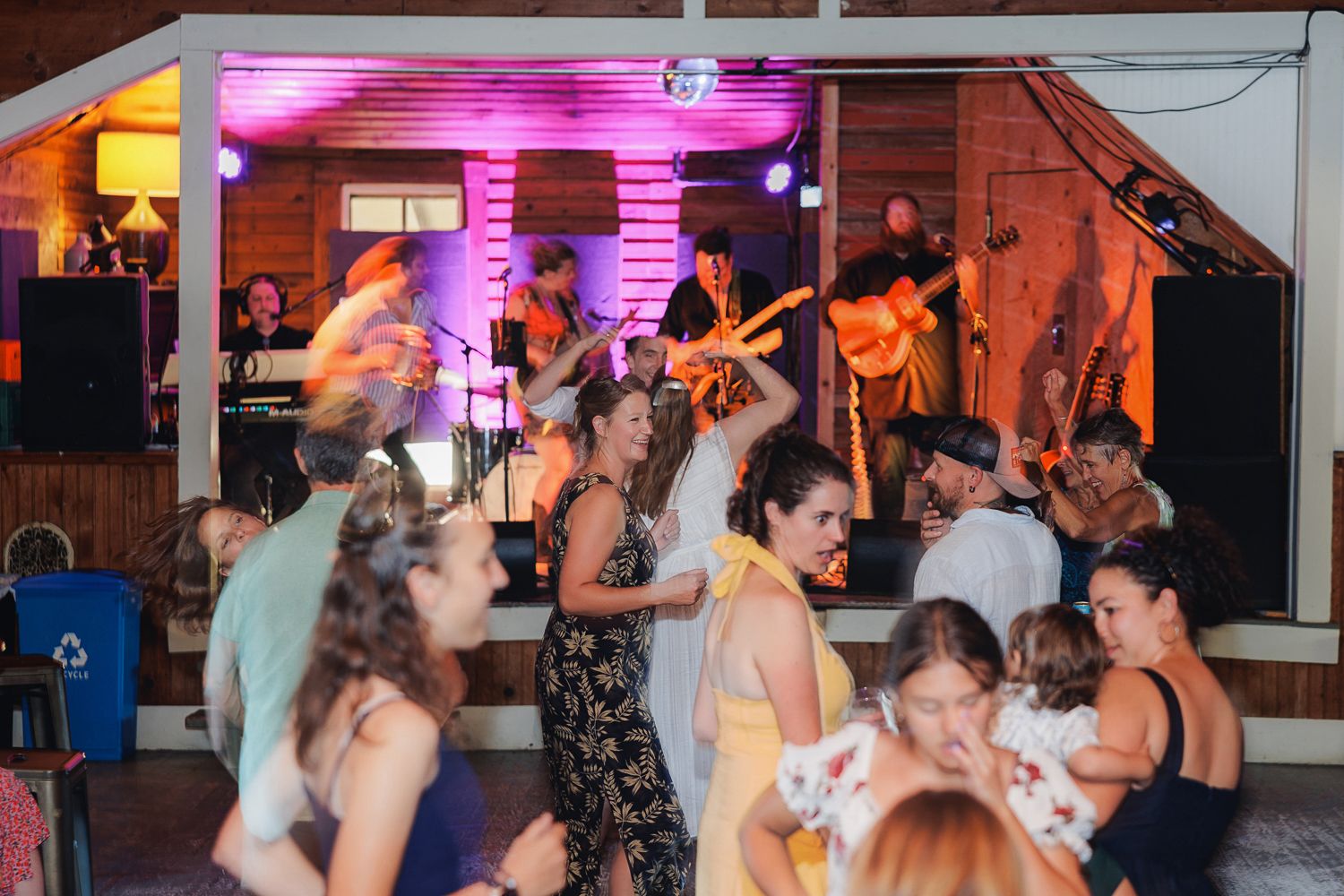 People dancing and enjoying live music at a party venue with pink lighting and a live band performing on stage.