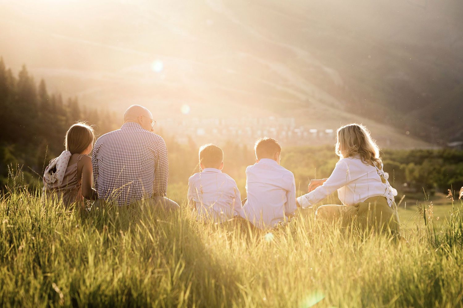 Group of people sitting in a sunlit meadow during golden hour as light streams through tall grass.
