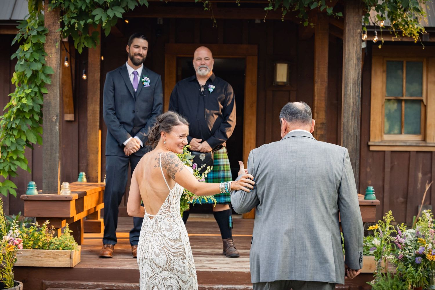 A couple dressed in wedding attire share a joyful moment on wooden steps with two guests watching from above.