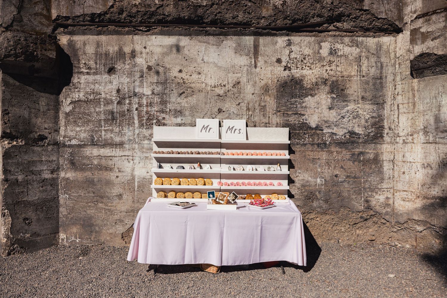 A tall stack of vintage books and records displayed on a white tablecloth against a weathered concrete wall.