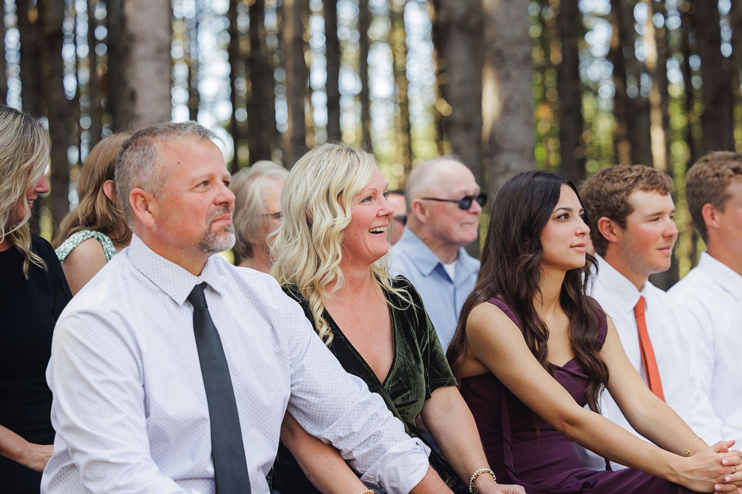 Wedding guests seated outdoors in a forest setting watching the ceremony.