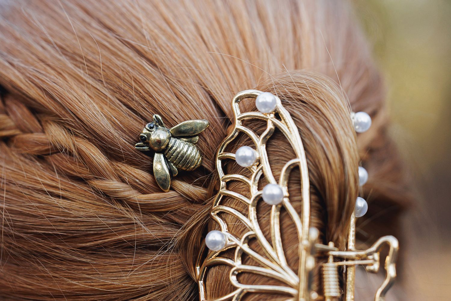 Bronze bee and gold butterfly hair accessories with pearl accents styled in a braided auburn hairstyle.