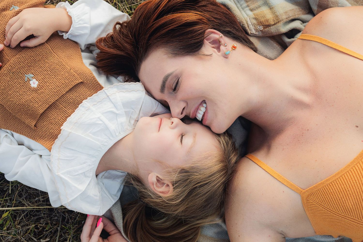 Mother and daughter lying on blanket sharing joyful moment outdoors.