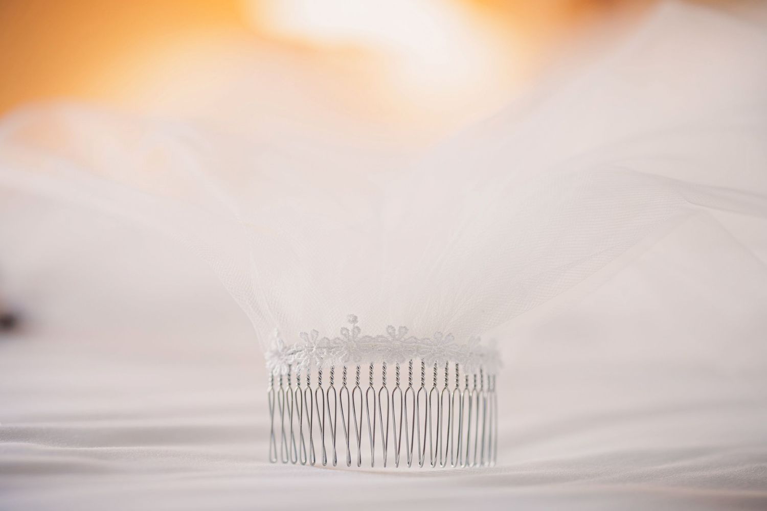 A silver metal hair comb or tiara with delicate prongs sits on a soft white surface in dreamy lighting.