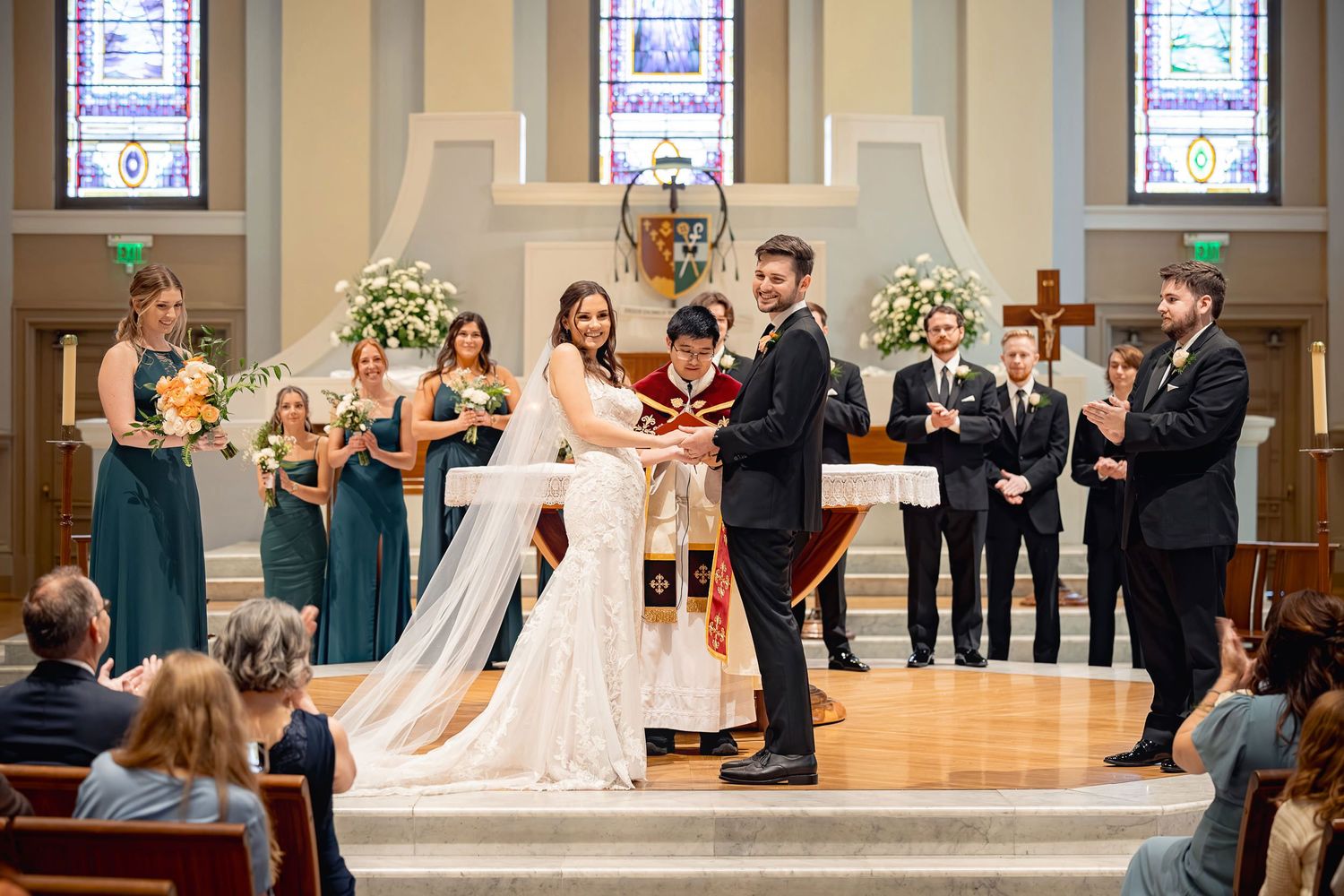 Wedding ceremony takes place inside a church with attendants and floral arrangements at the altar.