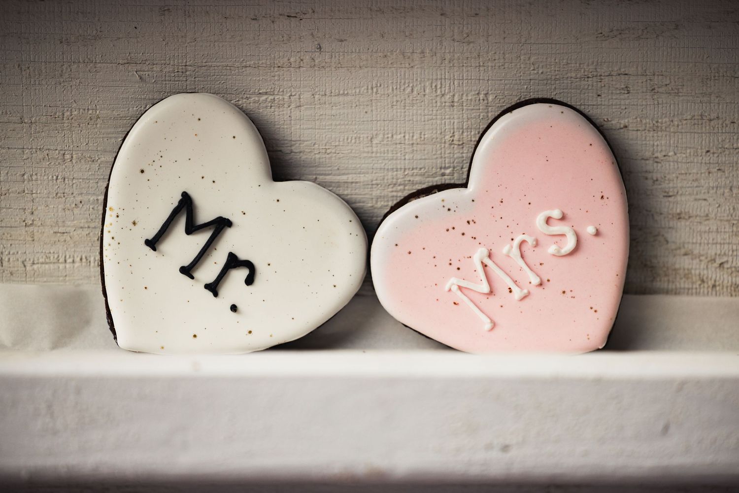 Two heart-shaped decorative stones with 'Mr.' and 'Mrs.' text sit on a white wooden shelf against neutral background.