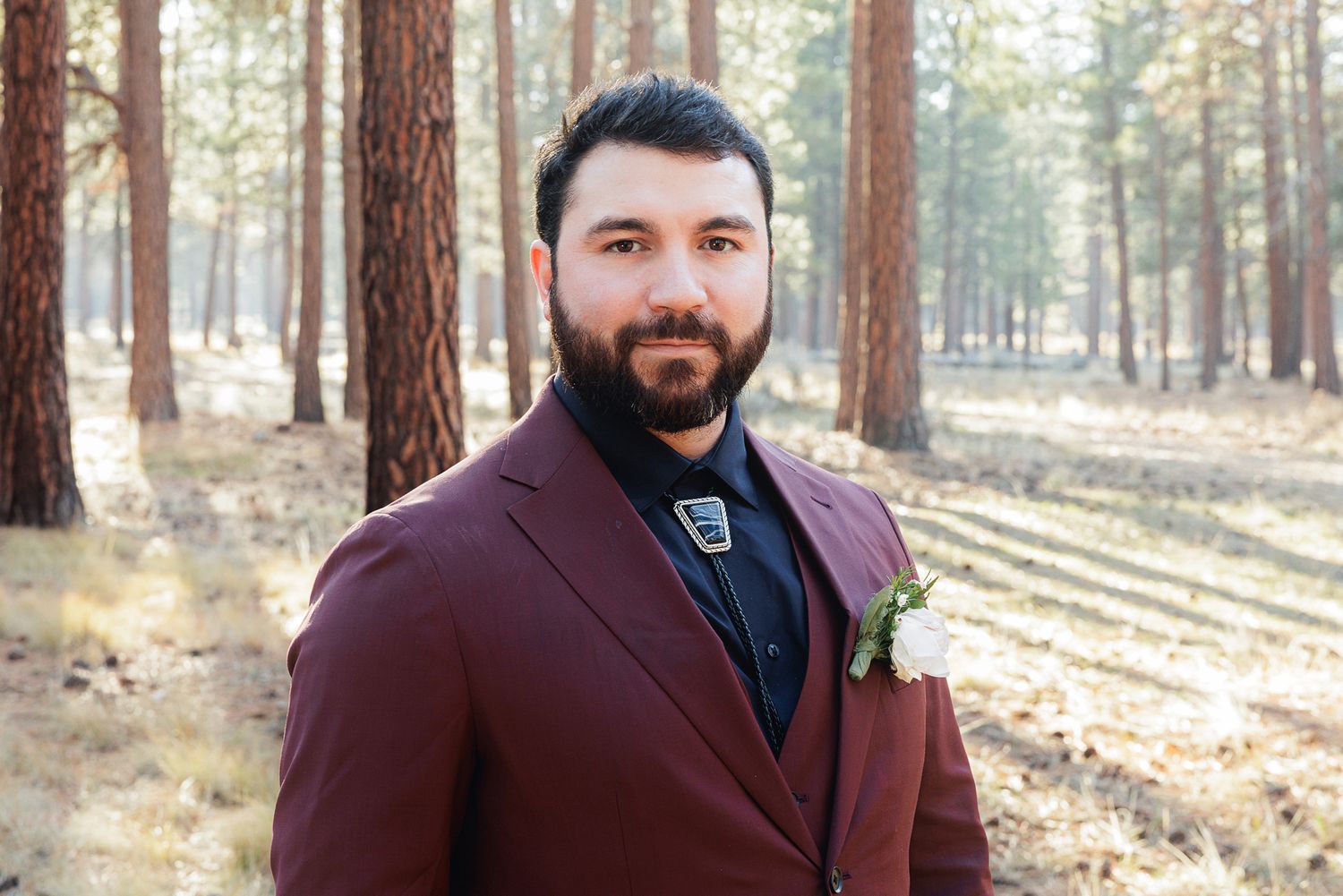 A wedding celebration unfolds in a pine forest with warm sunlight streaming through the trees.