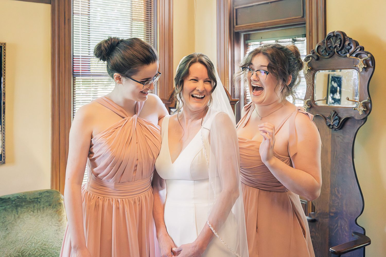 Five people in blush pink dresses share joyful candid moments during celebration preparations.