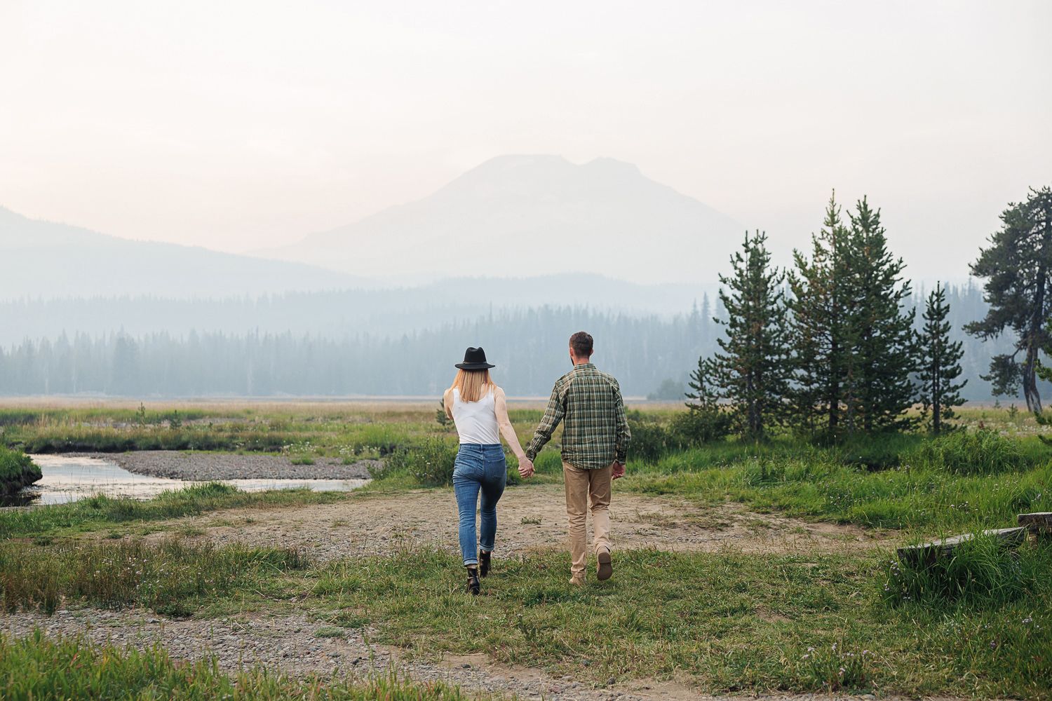 Two people walk along a scenic mountain path at sunset with sweeping valley views in the background.