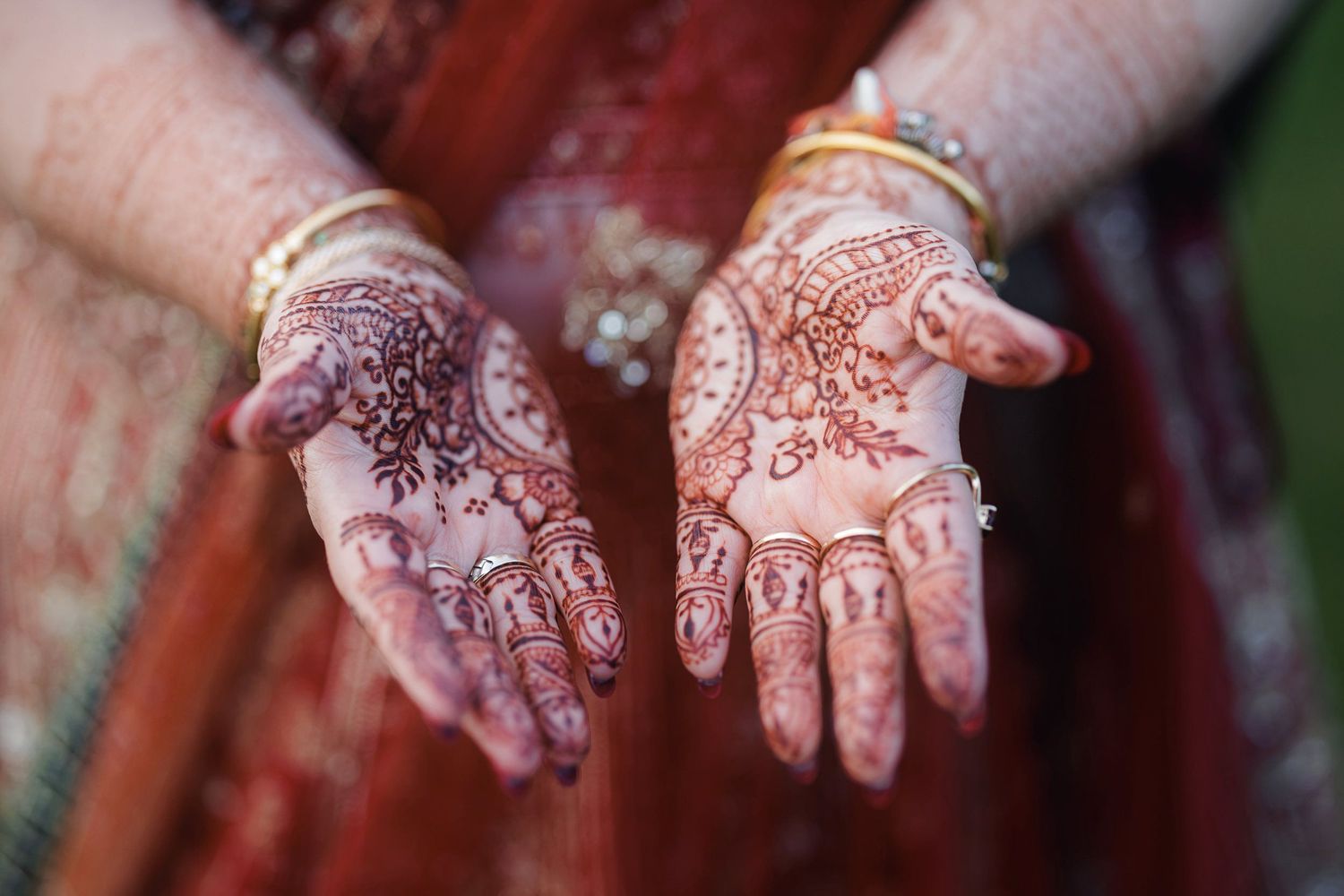 Woman displaying intricate henna mehndi designs on both palms, wearing gold bangles and a red traditional Indian outfit.