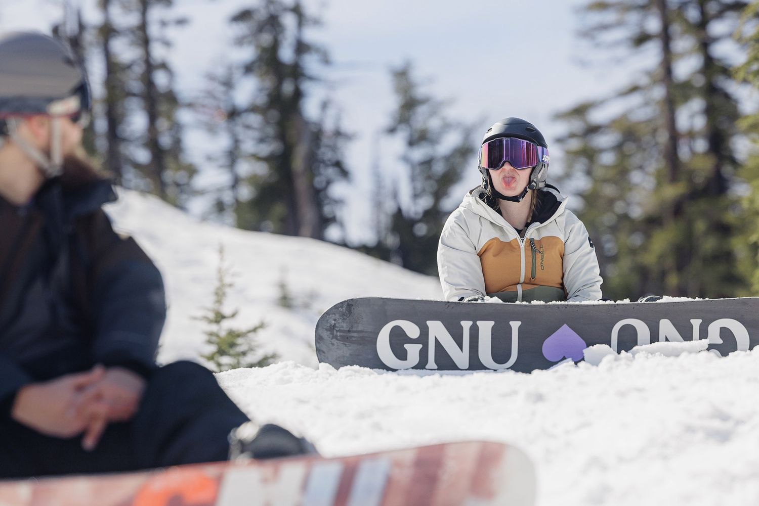 A snowboarder on a slope with a 'GNU' logo on the snowboard.