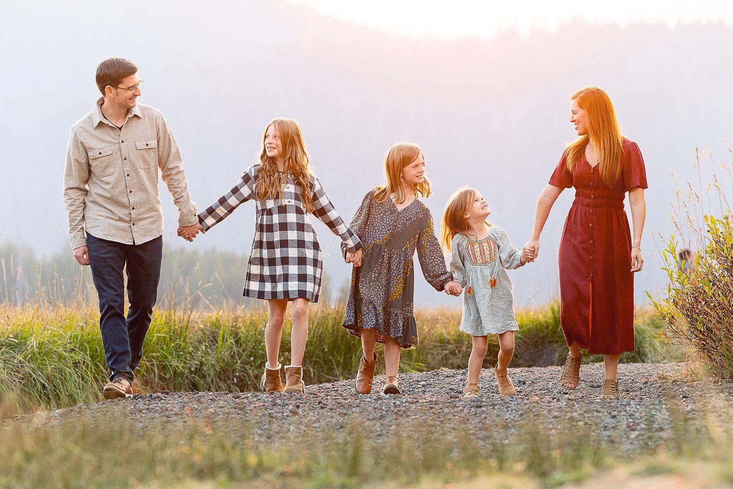 Group holding hands while walking together on a gravel path at sunset with mountains in the background.