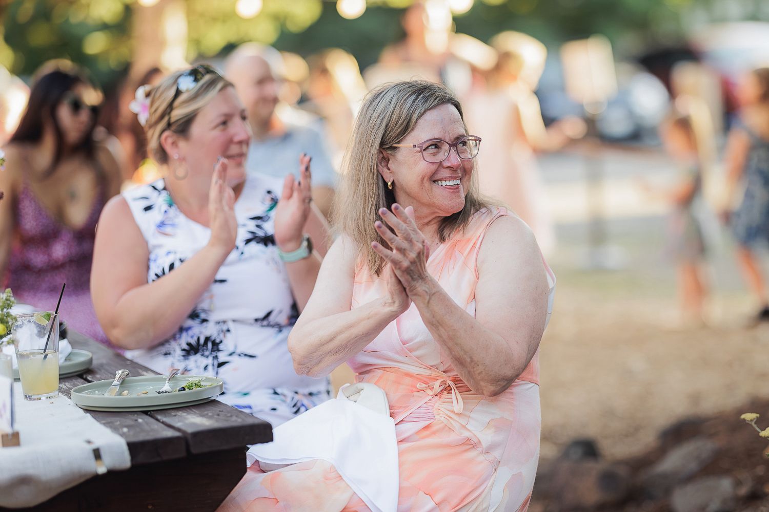 People clapping and laughing while seated at an outdoor table during a summer celebration event.