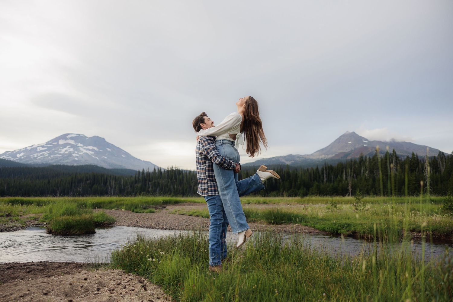 Dancing woman twirls joyfully against scenic mountain landscape with snow-capped peaks and green meadows.