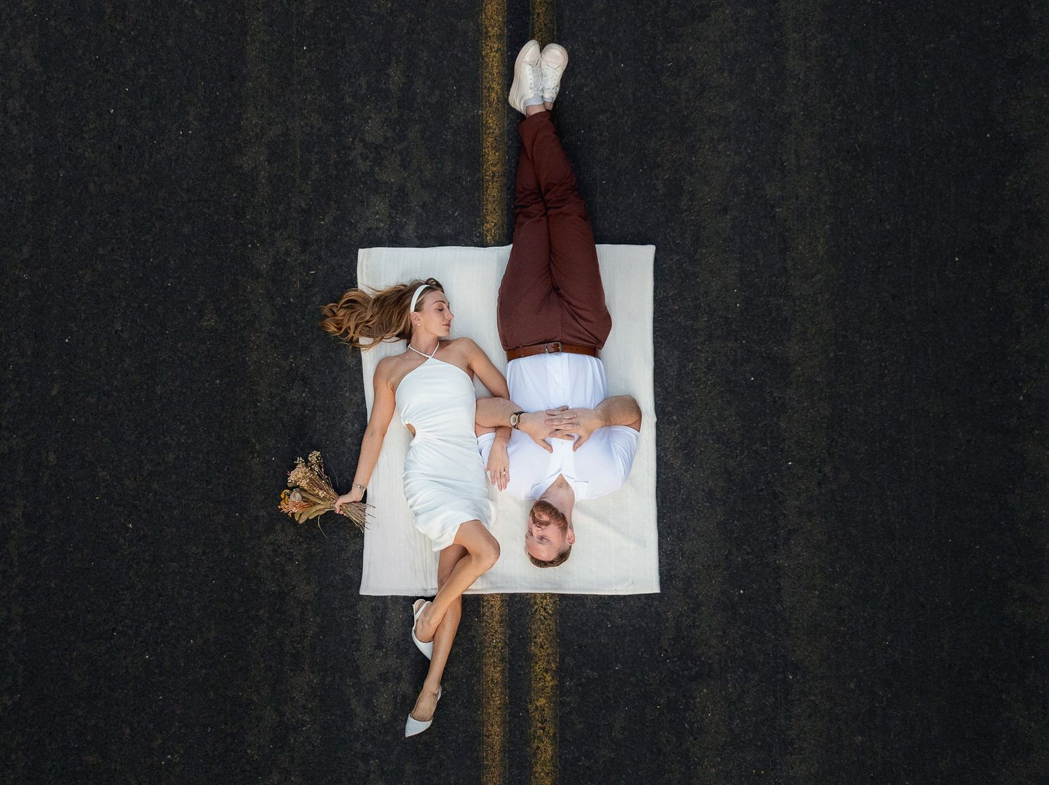 Overhead view of people lying on white surface wearing contrasting burgundy and white outfits on dark background.