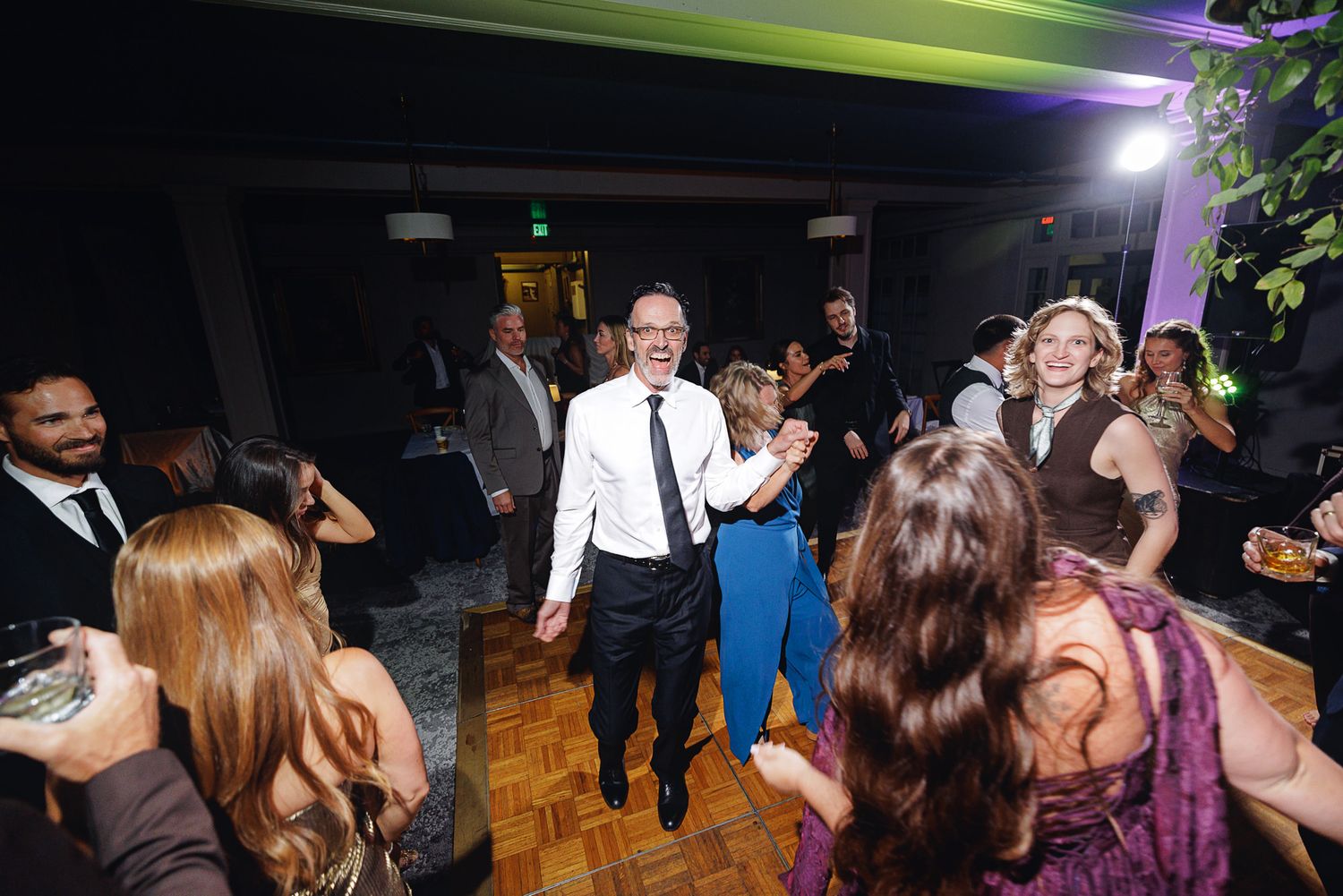 Guests dancing and celebrating at an elegant indoor wedding reception on a wooden dance floor.