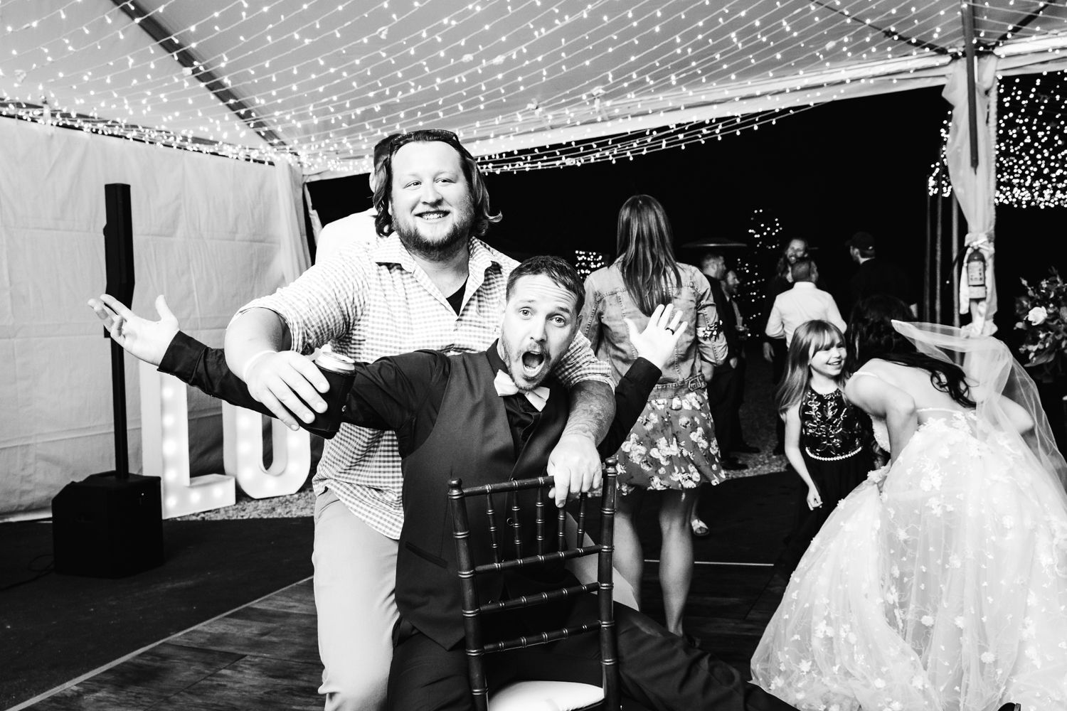 A black and white photo of a wedding reception dance party under string lights.