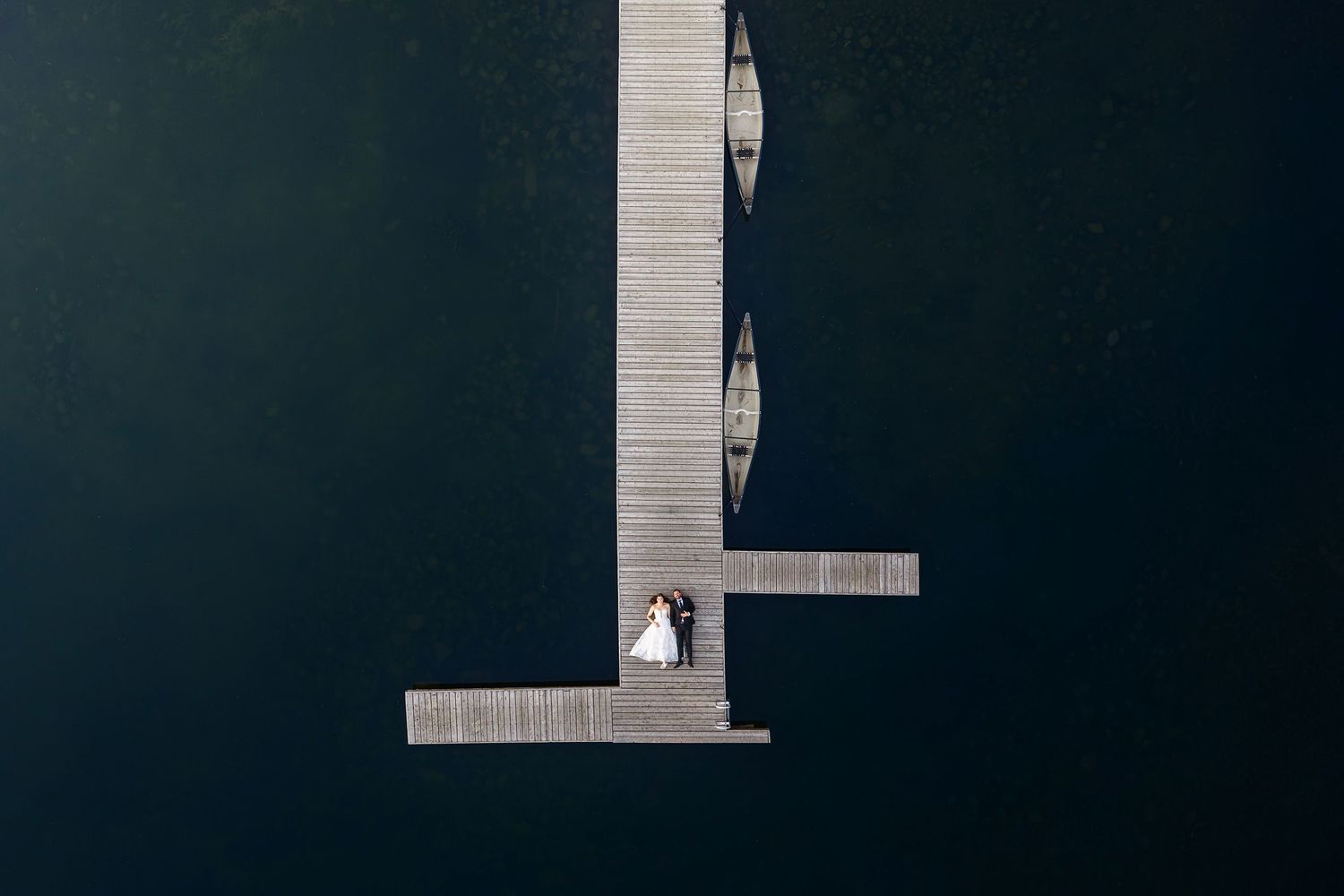 Aerial view of a bride and groom standing on a wooden dock surrounded by dark water.