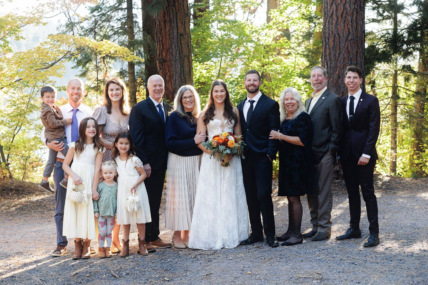 Family group portrait at outdoor woodland wedding with bride and groom surrounded by relatives among tall trees.