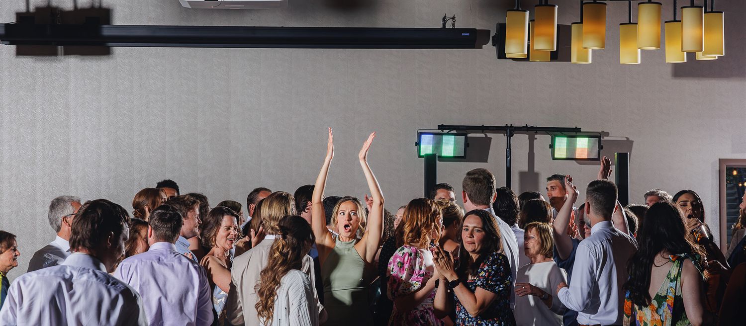 Guests dancing and celebrating at a lively indoor party event with warm lighting and a crowded dance floor.