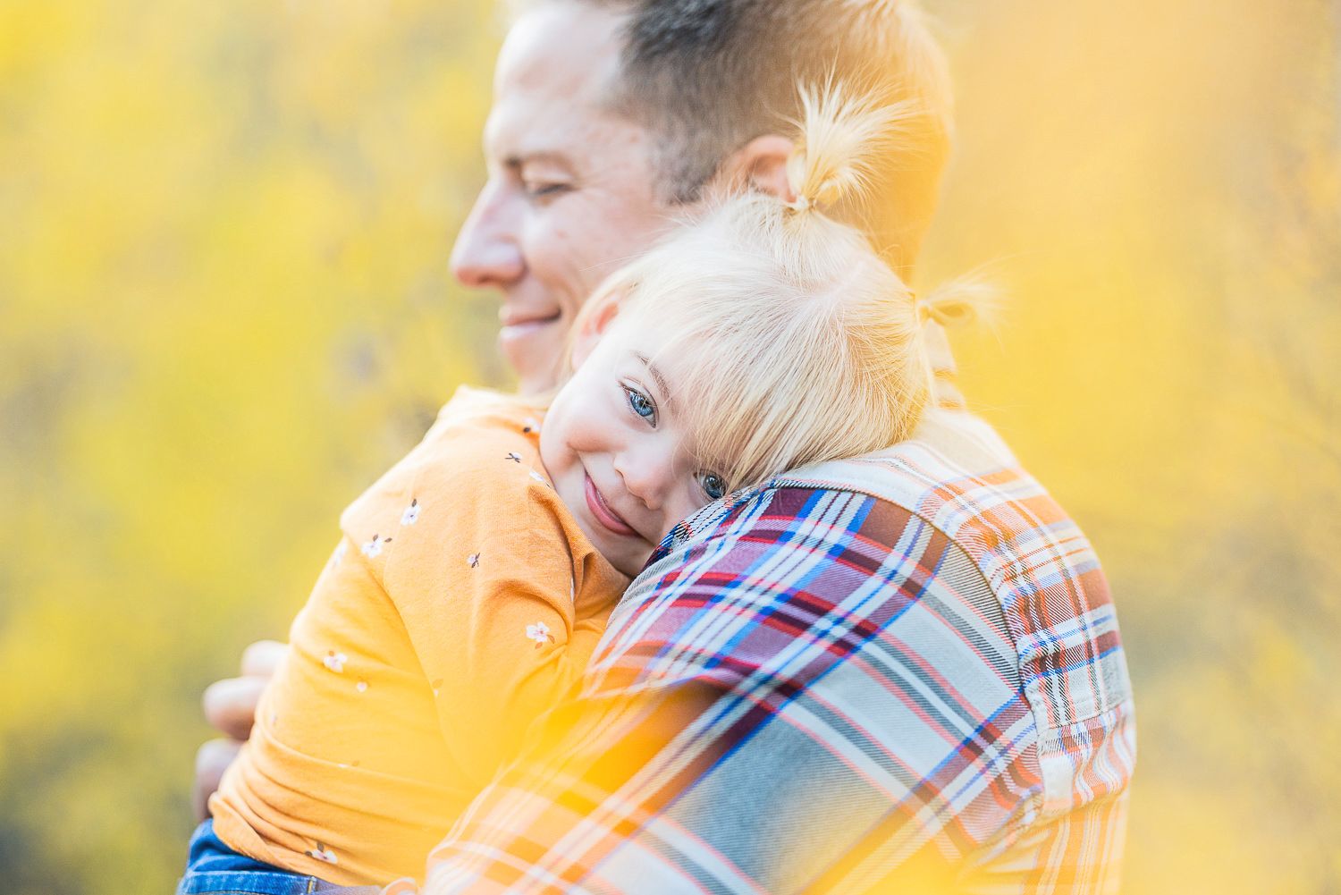 A warm embrace shared between an adult and child against a soft golden yellow autumn background.