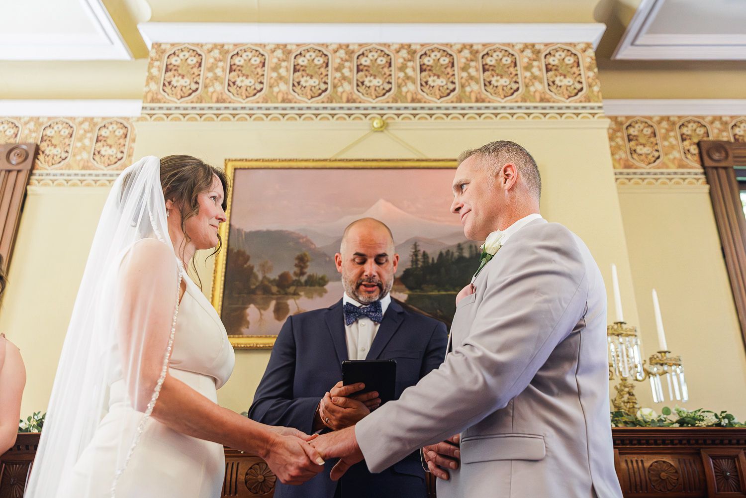 Wedding party gathers and celebrates together inside an elegant venue with ornate gold decor and columns for photos.