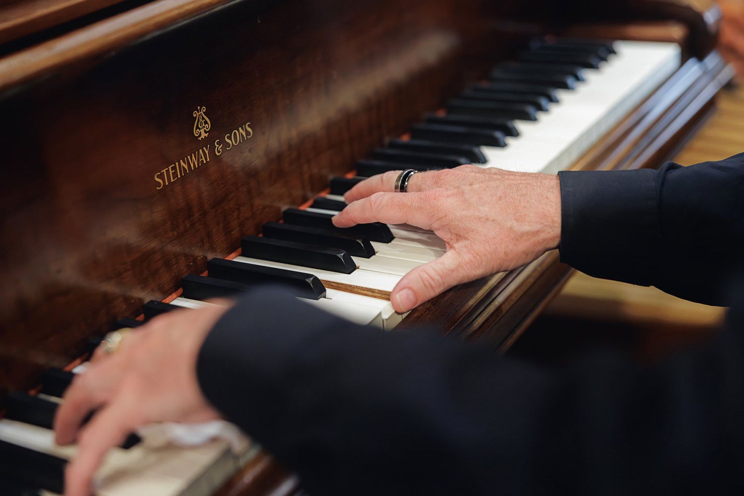 Close-up shots of hands playing piano keys on a black grand piano in dramatic lighting.