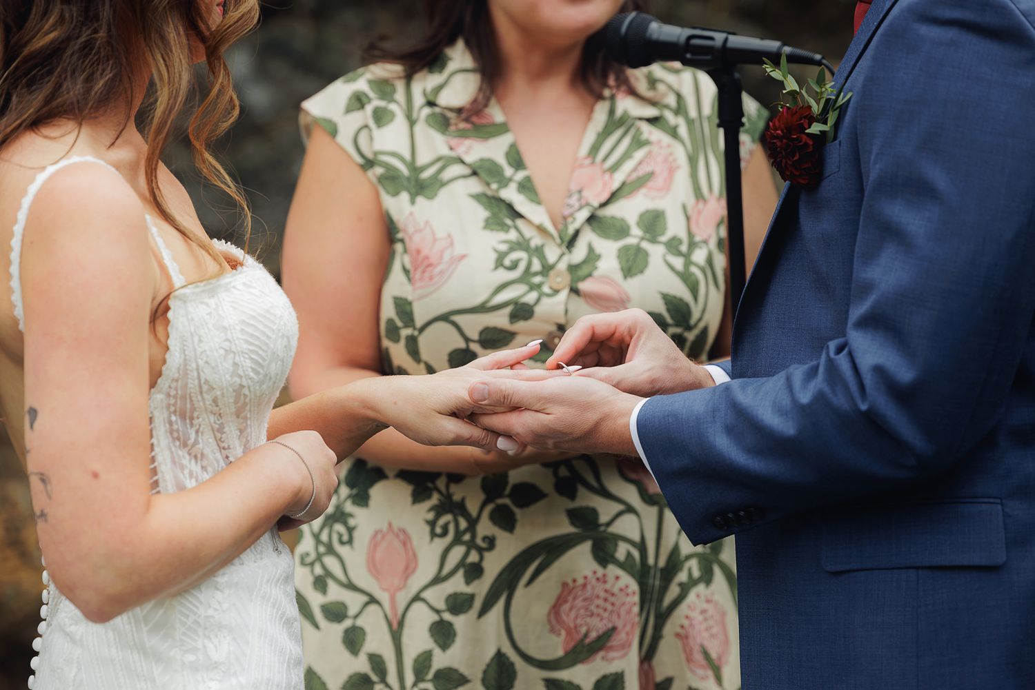 Couple exchanges wedding rings during ceremony in front of floral backdrop.