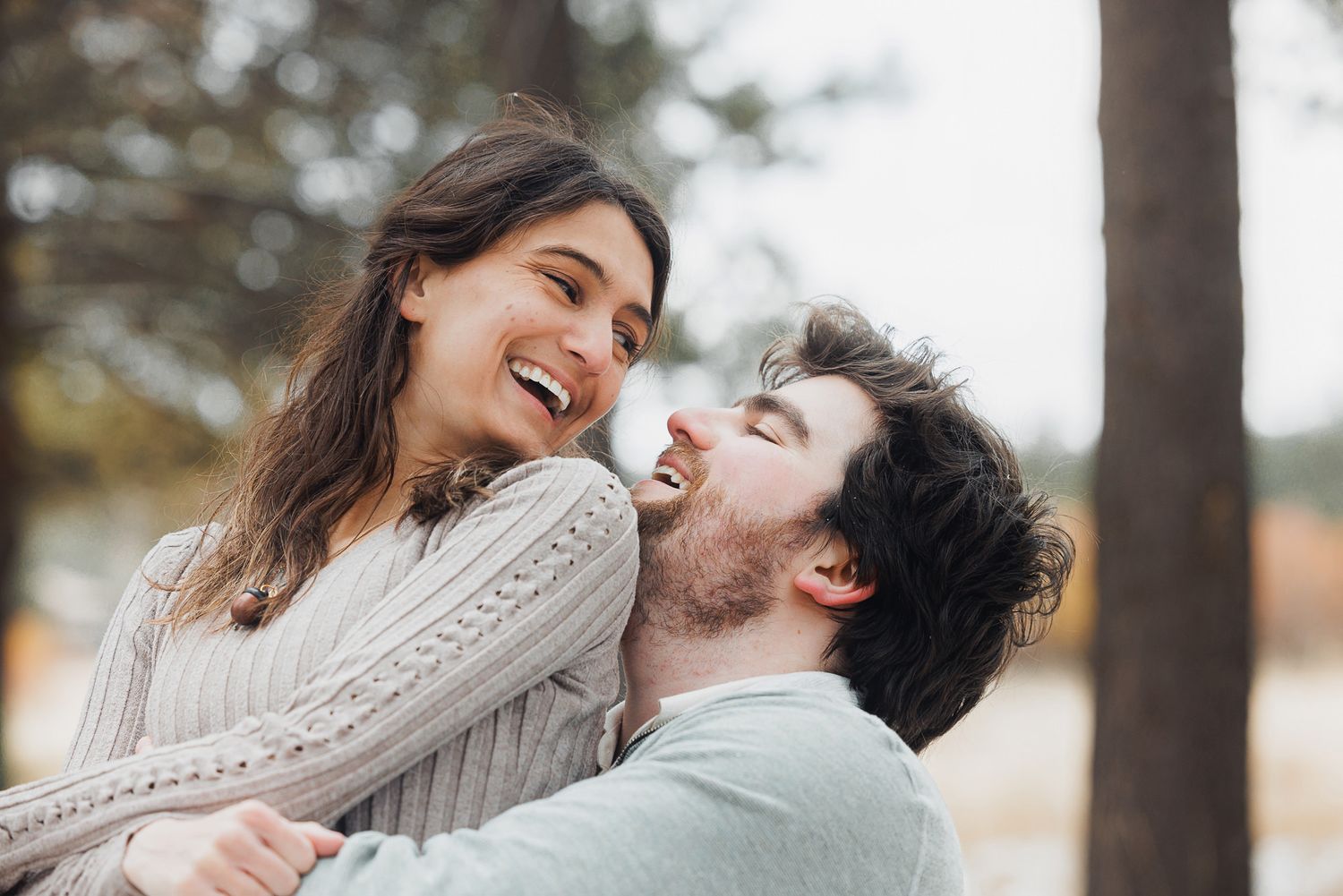 Romantic couple laughing and embracing outdoors in matching beige sweaters during an autumn photoshoot.