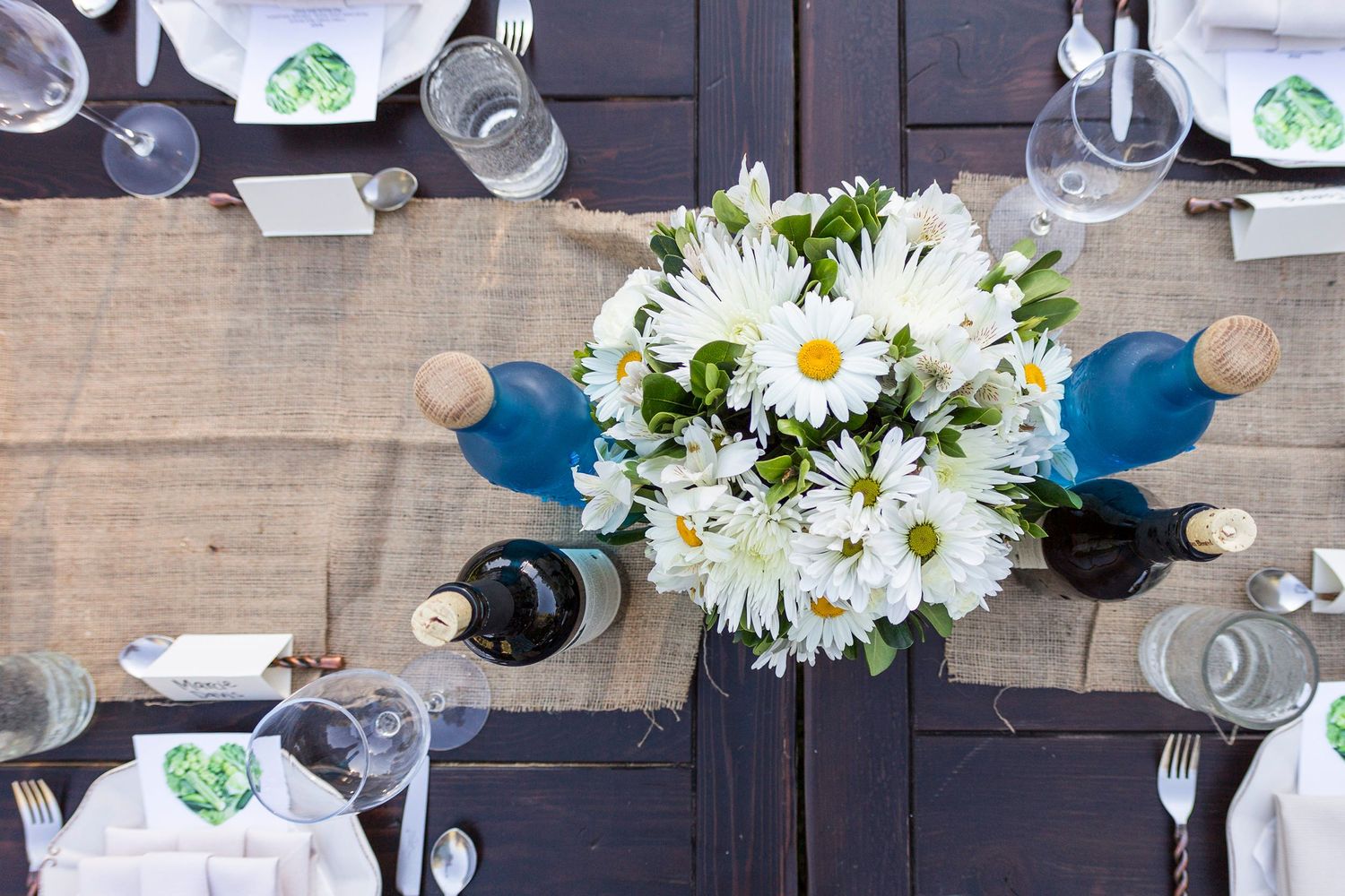 White daisy flower centerpiece on rustic wooden table with place settings.