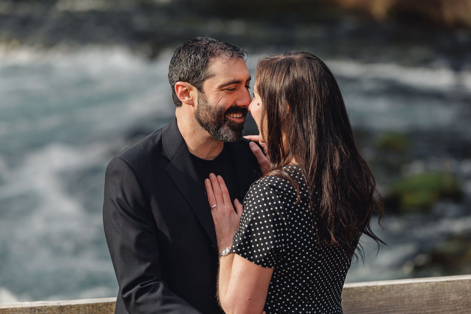 Couple sharing a romantic moment near a rushing river, smiling at each other outdoors.