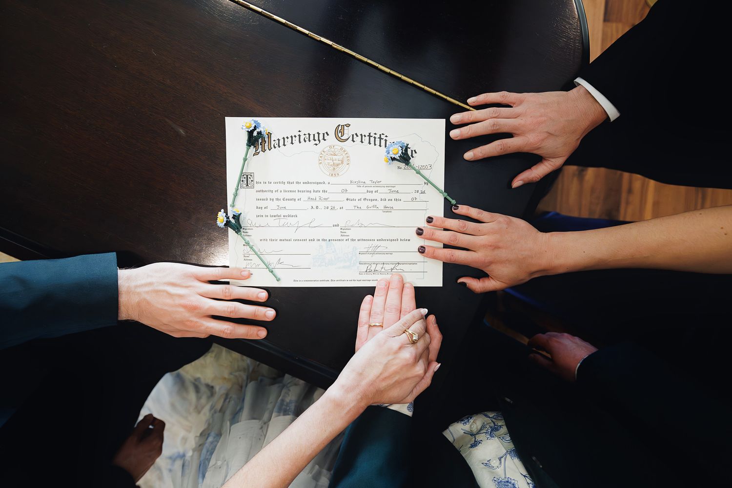 Hands touching a marriage certificate on a dark wooden table during a wedding ceremony.