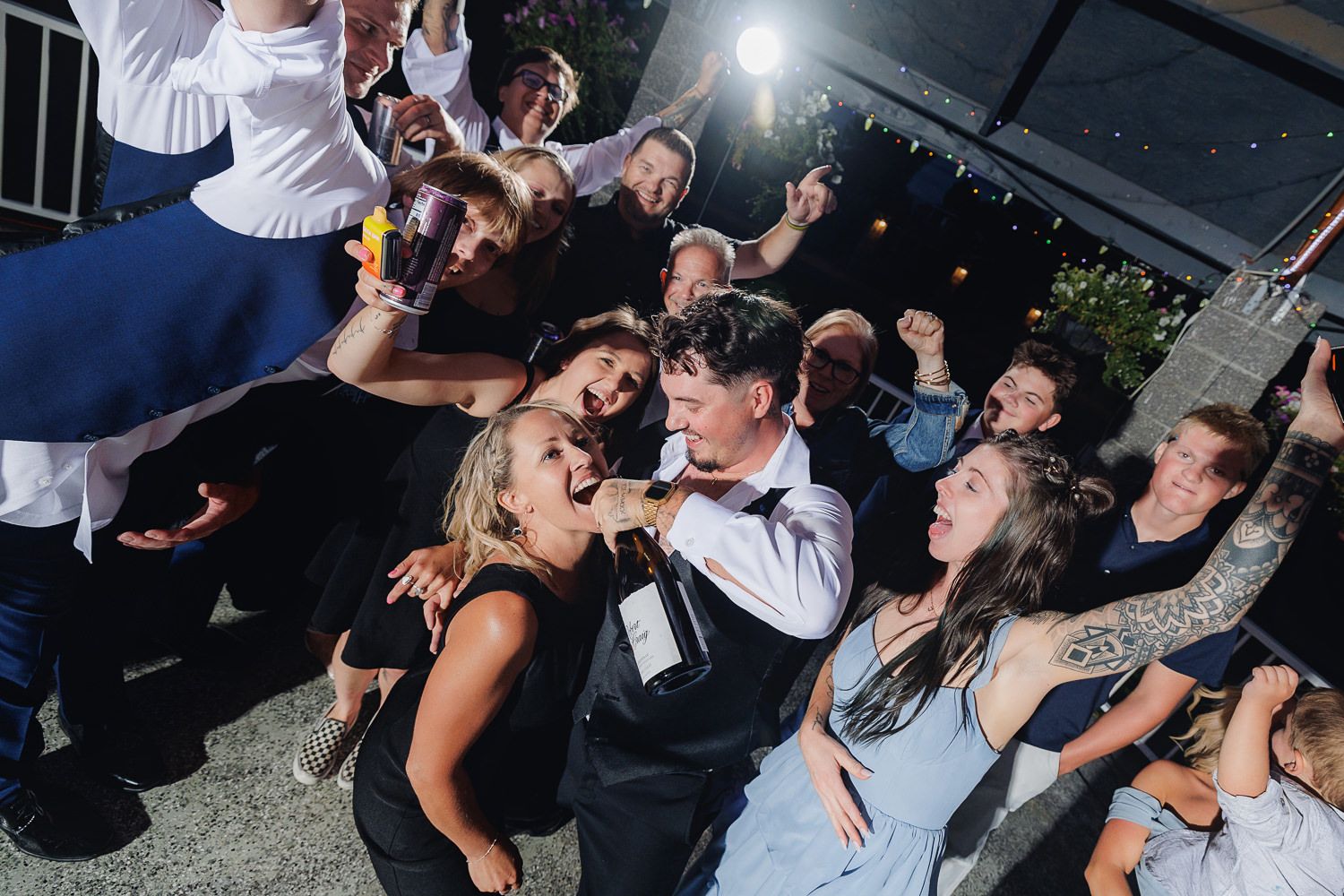 Energetic crowd dances and sings together at a lively wedding reception party with dramatic lighting.