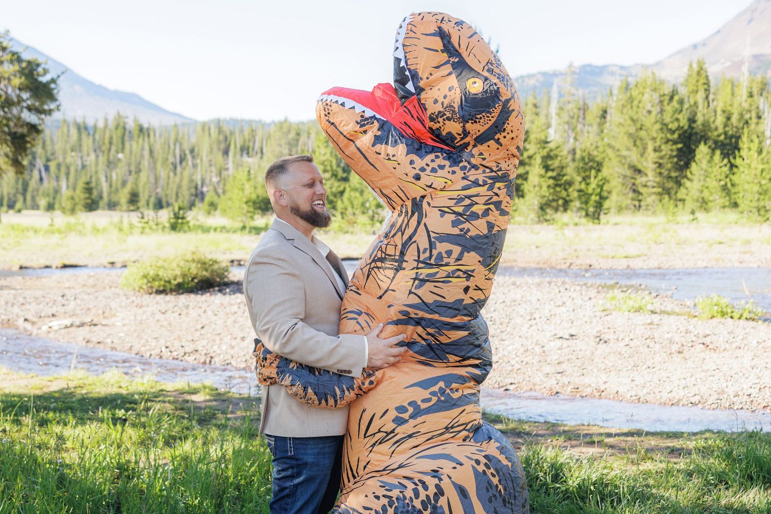 A couple hugs while wearing colorful patterned blankets in front of scenic mountain and forest views.