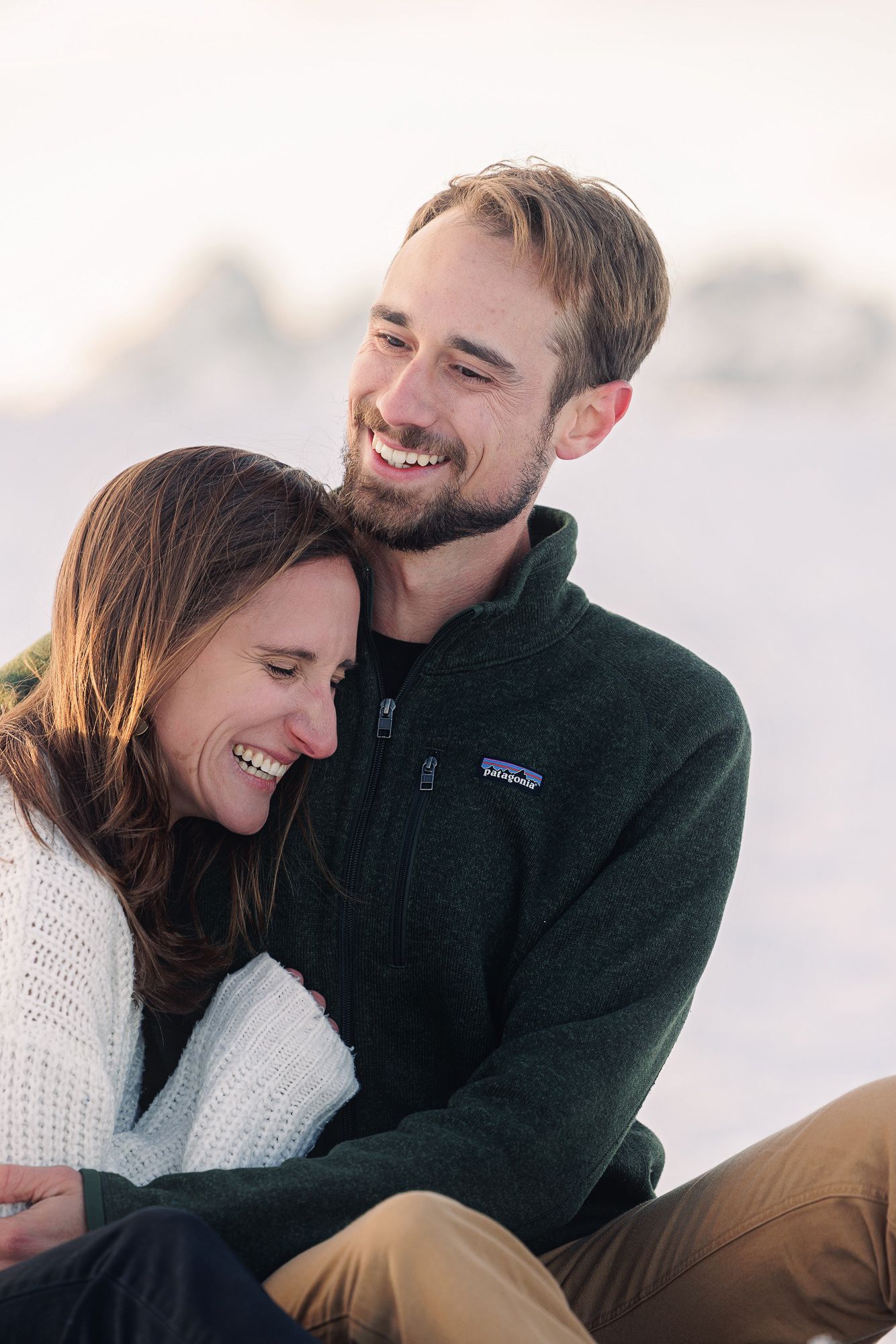 Happy couple smiling and embracing outdoors in winter, man in green Patagonia fleece, woman in white sweater.