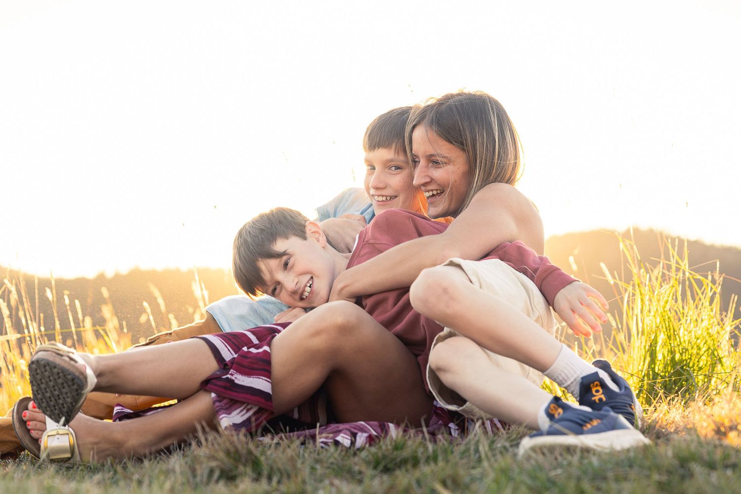 A joyful group embrace while sitting in tall grass during golden hour.
