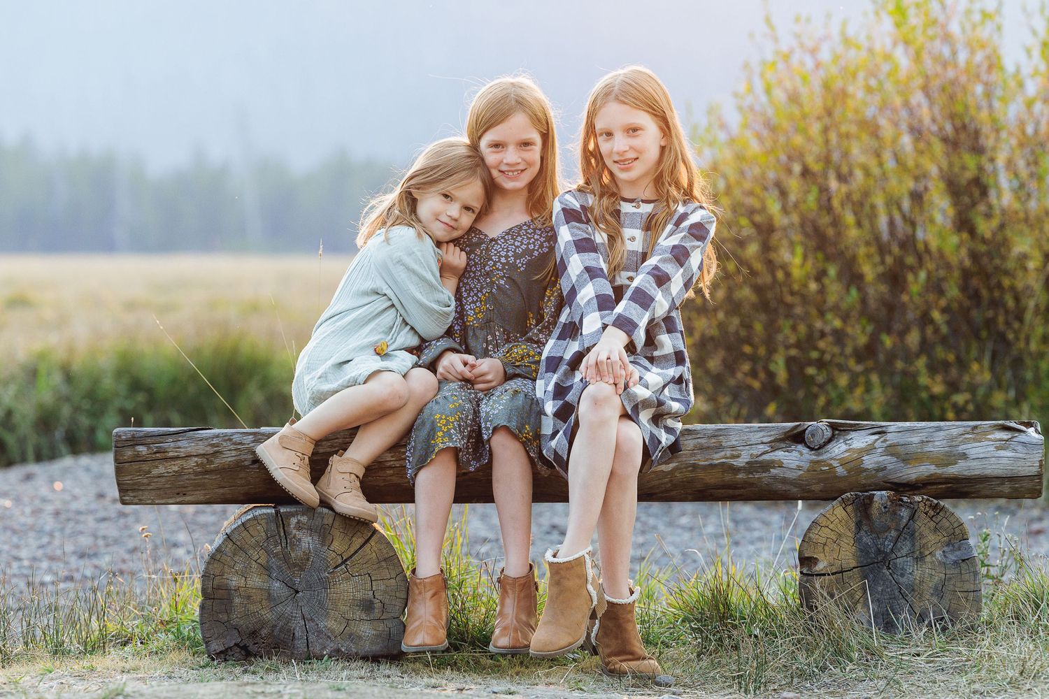 Three siblings sitting together on rustic wooden bench in nature.