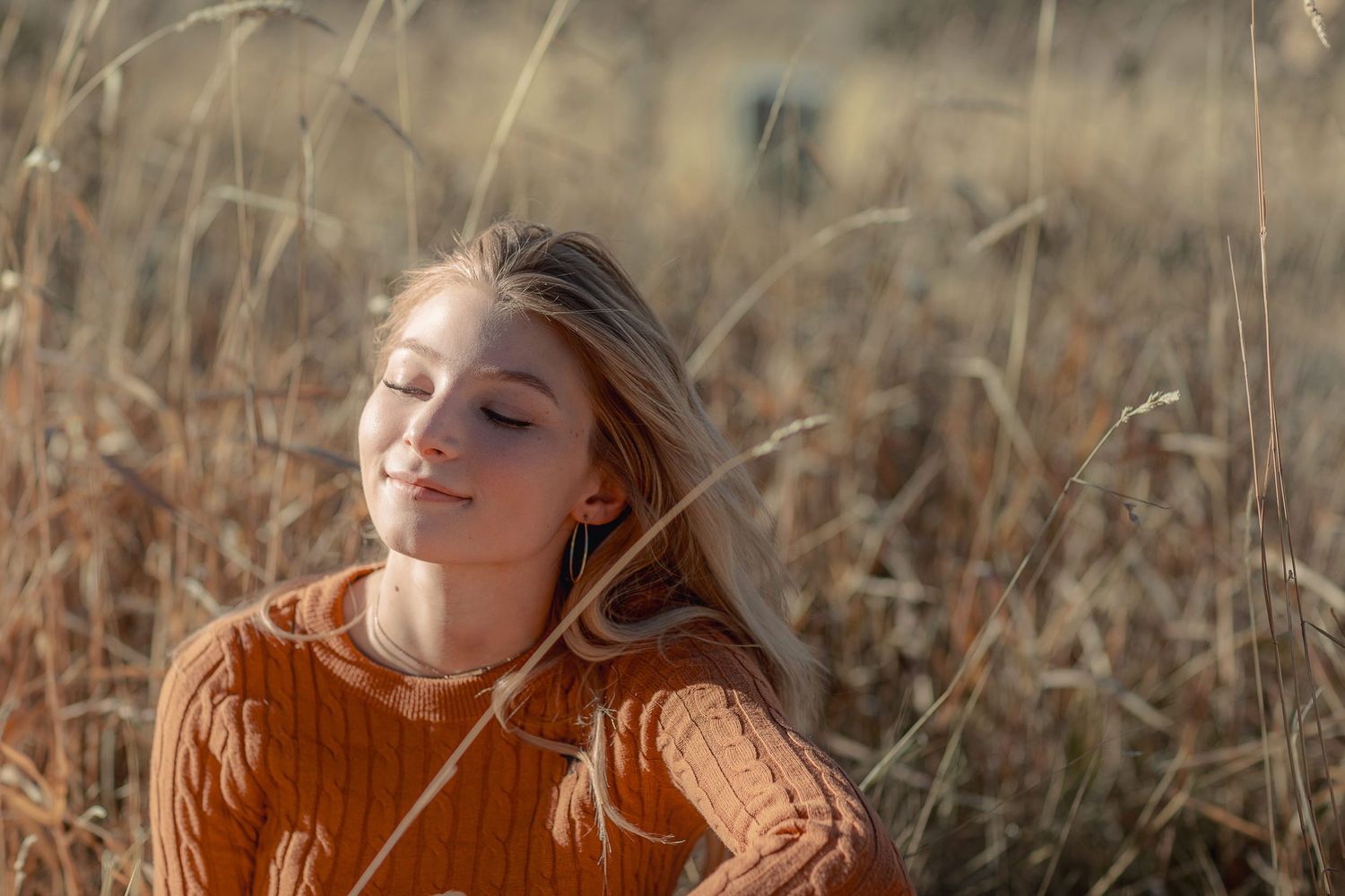 A dreamy portrait in golden wheat fields wearing an orange sweater.