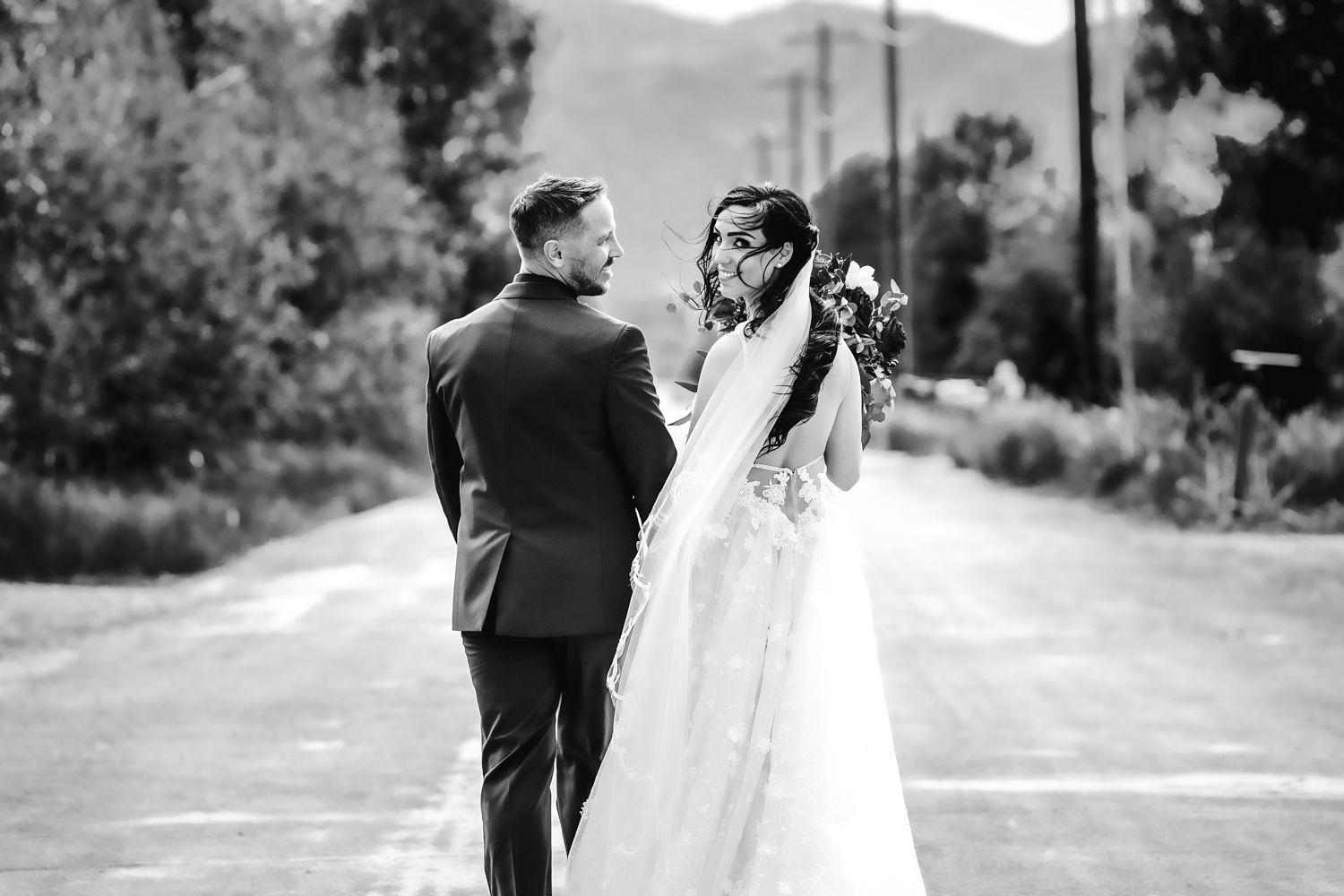 A black and white photo captures a couple sharing a special moment on a rural road with mountains in the distance.