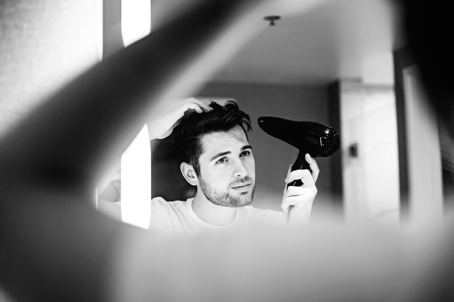 Black and white reflection in mirror through geometric shapes shows a person styling their hair.