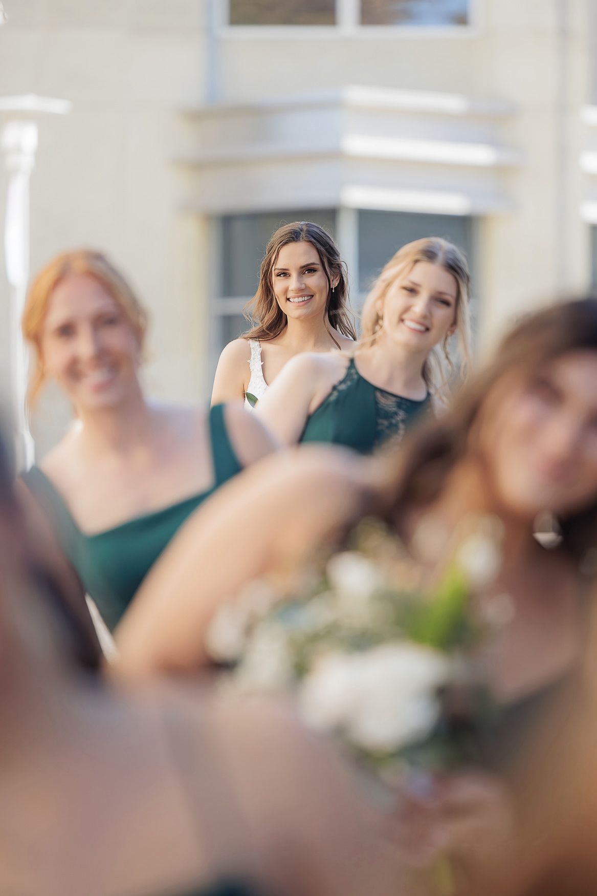 Bridesmaids wearing matching emerald green dresses smile during wedding celebration with soft focus effects.