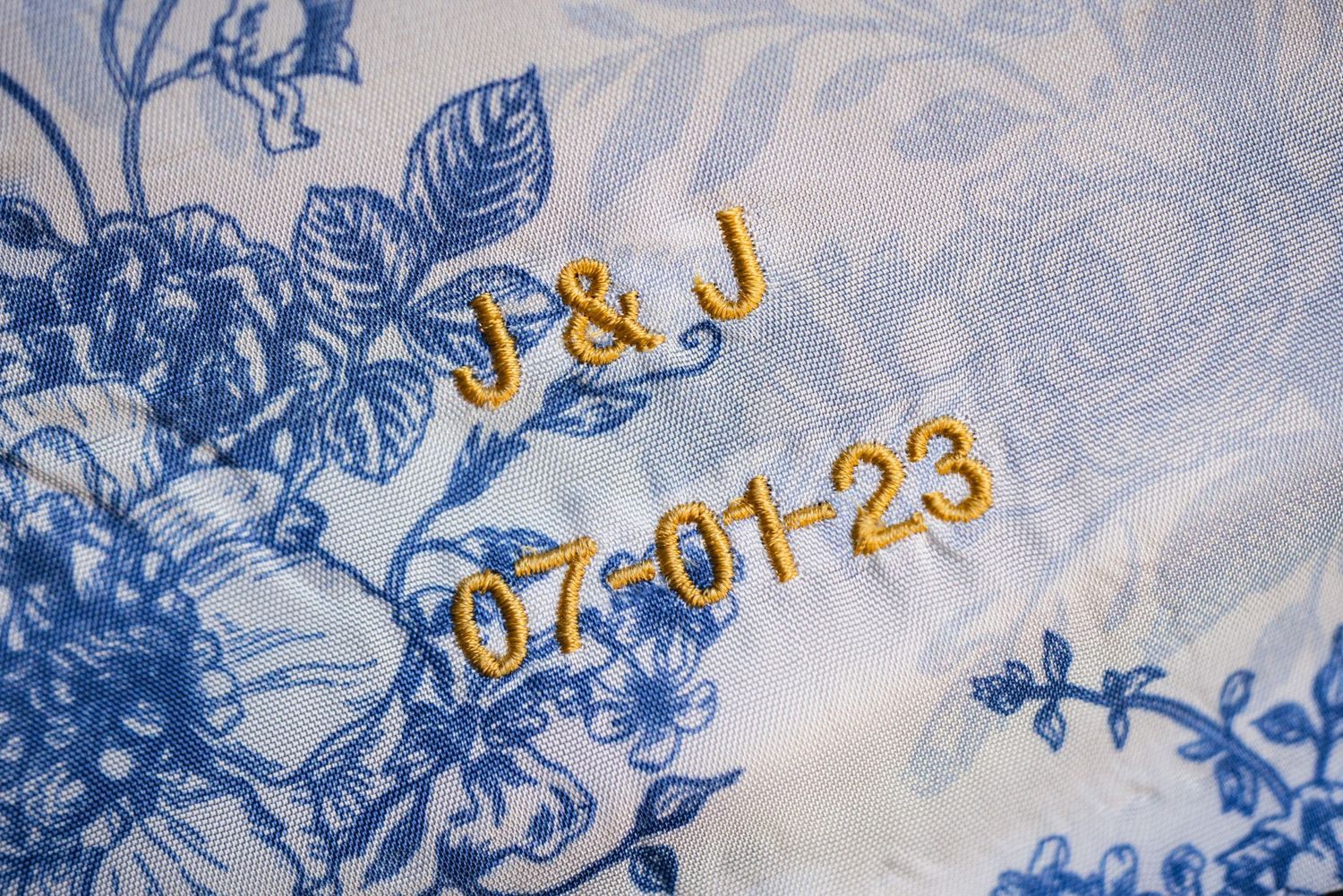 Blue floral pattern fabric with gold embroidered initials and date numbers in an elegant design.