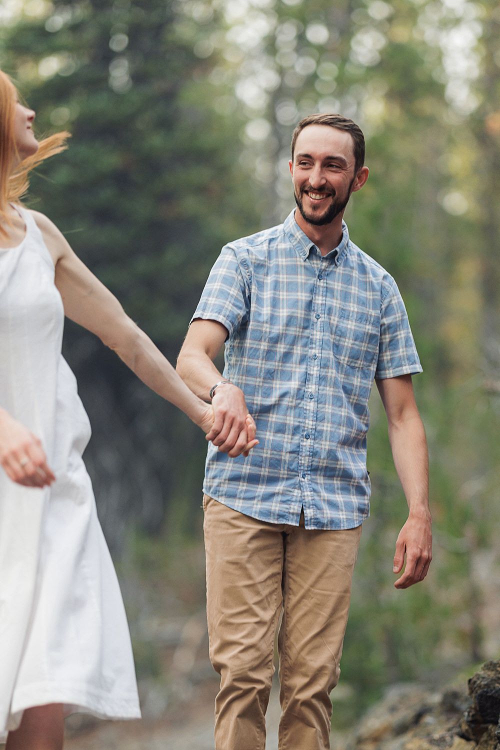 A couple walking outdoors in casual attire sharing a playful and candid moment in a natural setting.