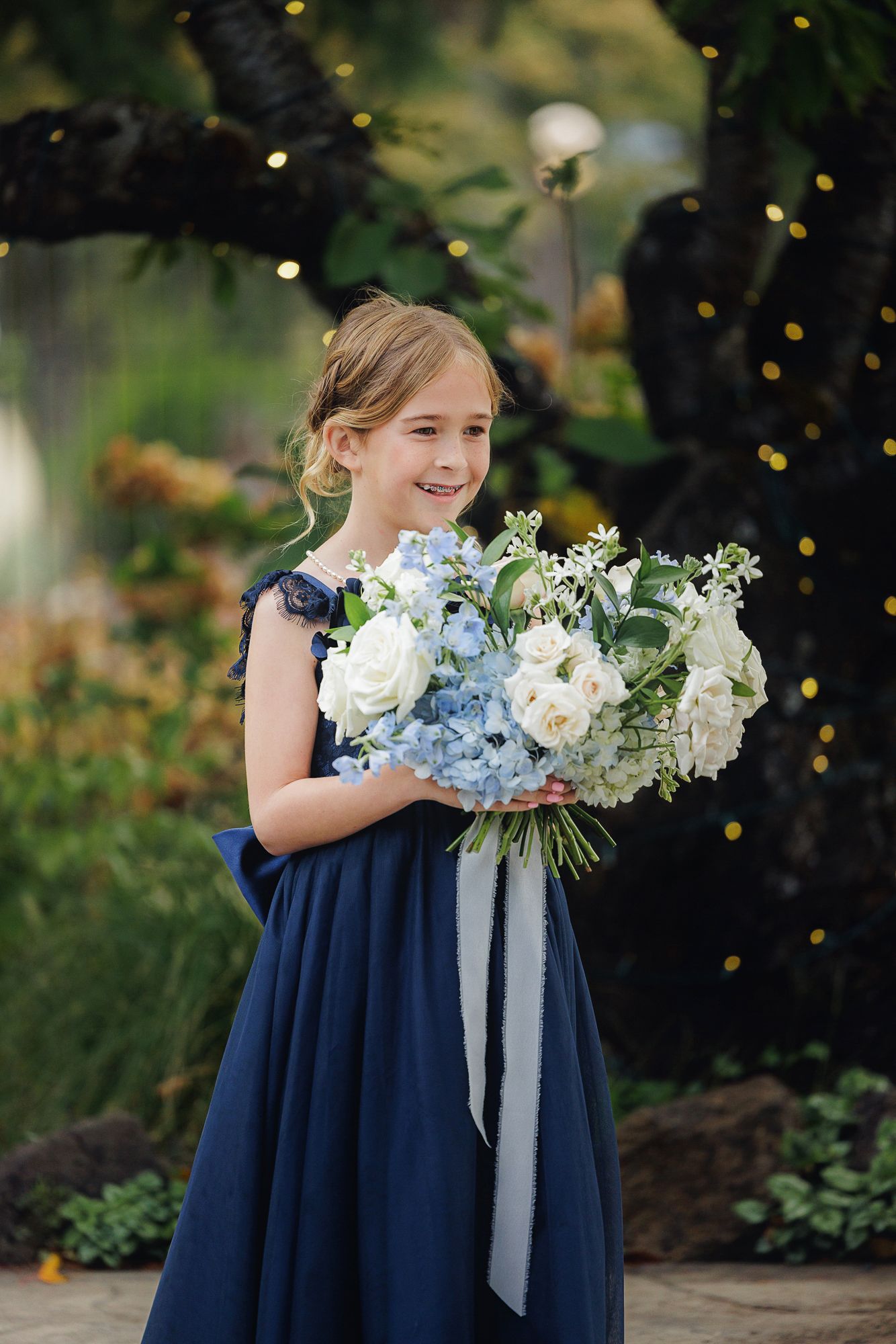 Row of navy blue dresses with elegant white and blue floral bouquets against a garden backdrop.