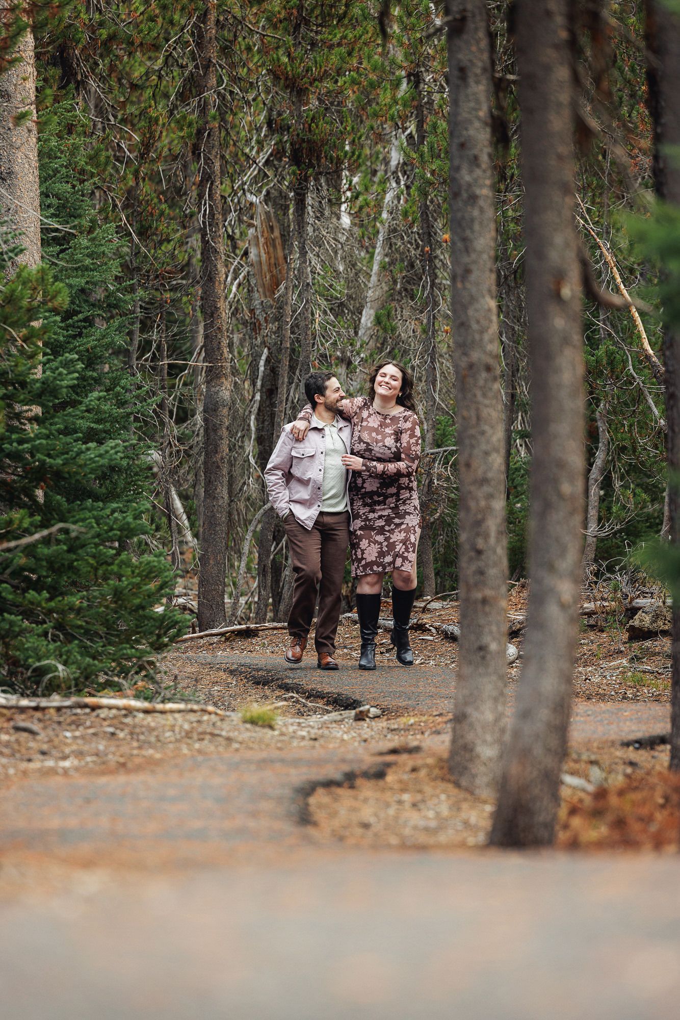 A couple shares a romantic moment while walking together through a wooded forest trail on an autumn day.
