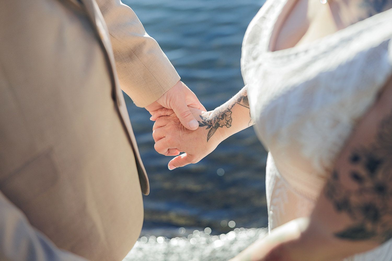 Two hands exchanging wedding rings during an outdoor beach ceremony with blue ocean water visible in the background.