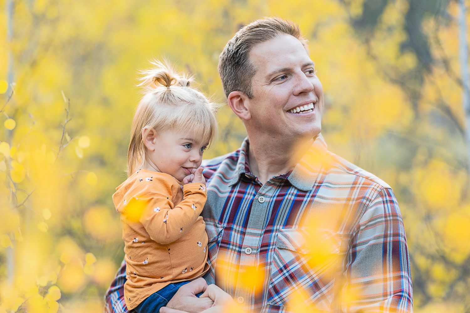 Parent and young child share a joyful moment together surrounded by golden yellow autumn foliage.