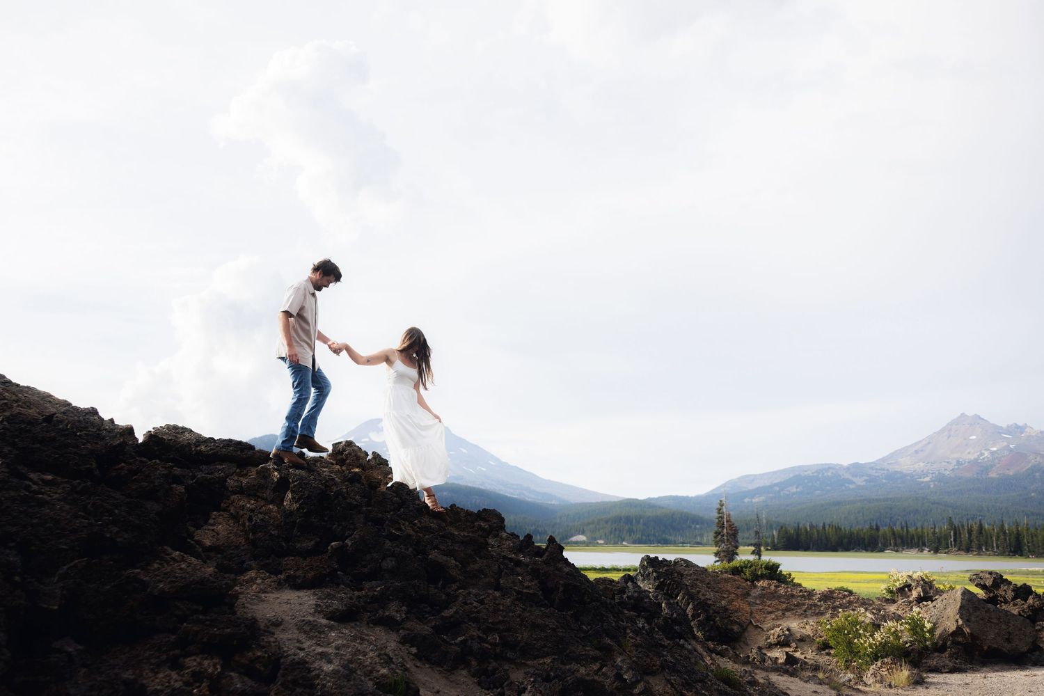 Person sits on rocky mountain edge overlooking scenic mountain lake landscape at sunset.