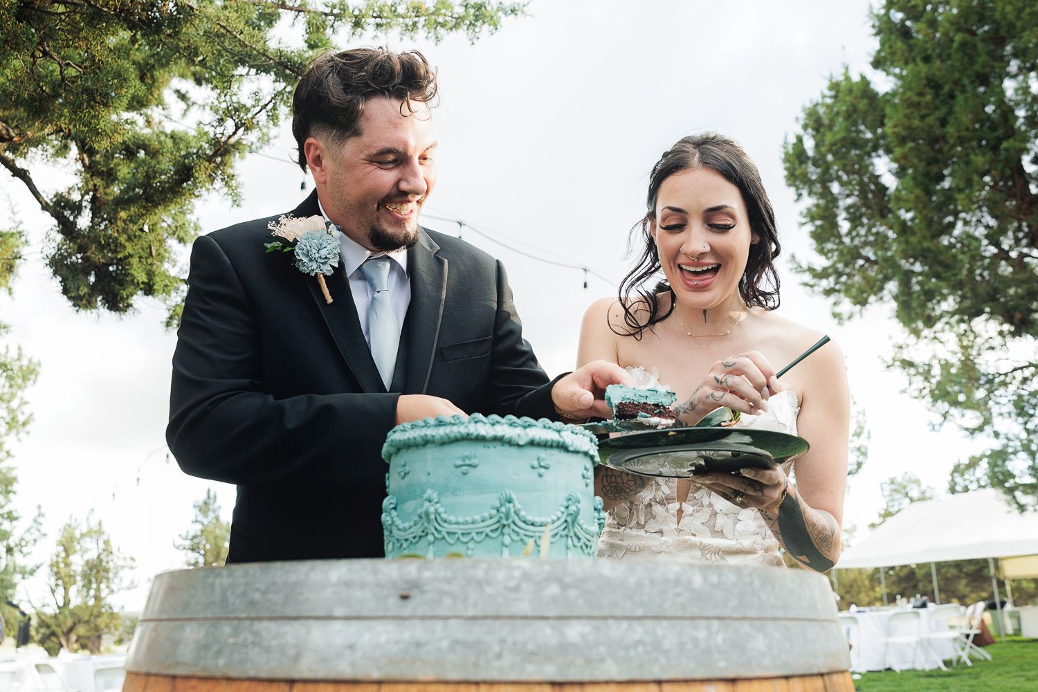A couple shares a joyful moment together while sitting outdoors on a stone wall surrounded by greenery.