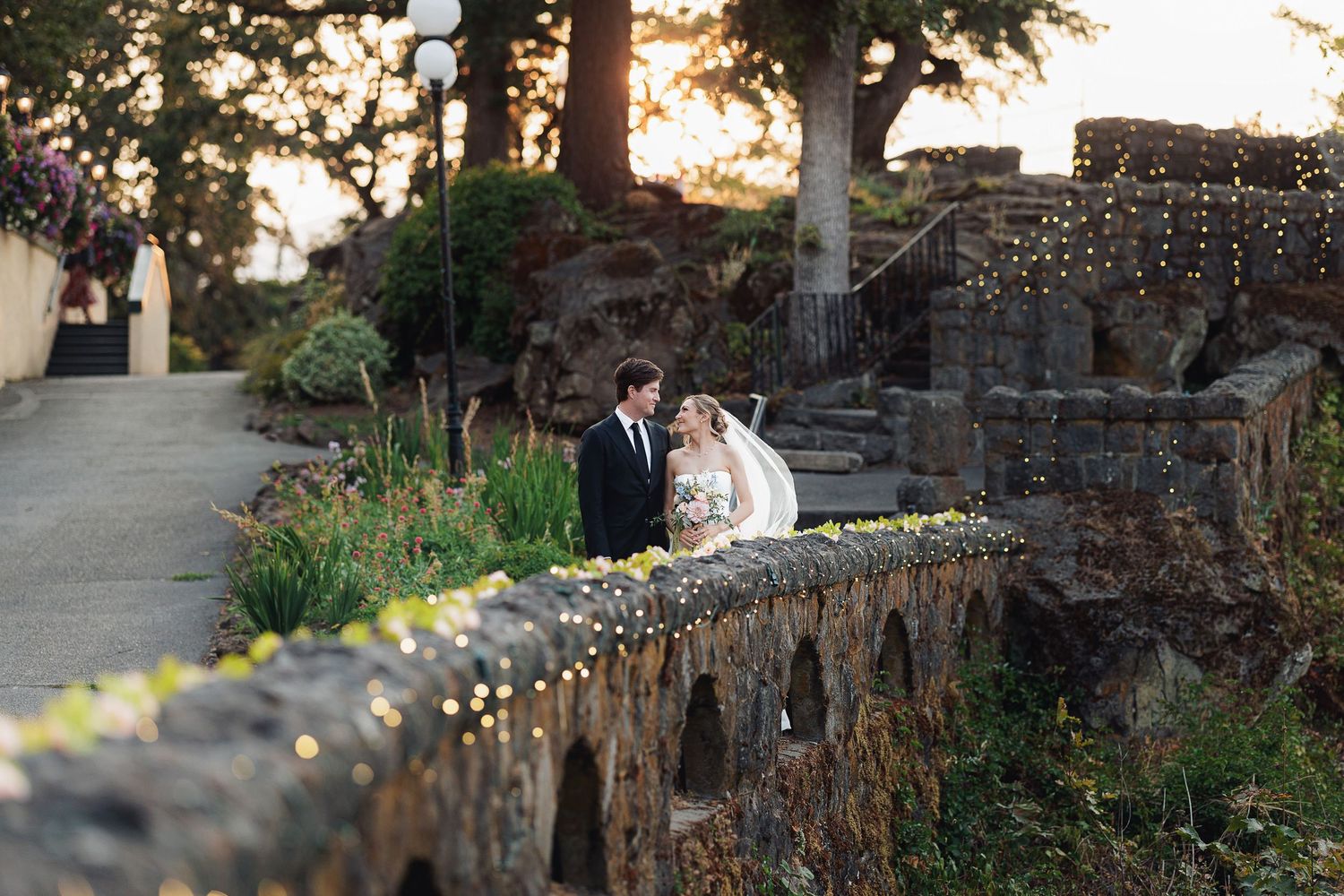 Bride and groom share a romantic moment on a stone bridge at a garden wedding venue at golden hour.